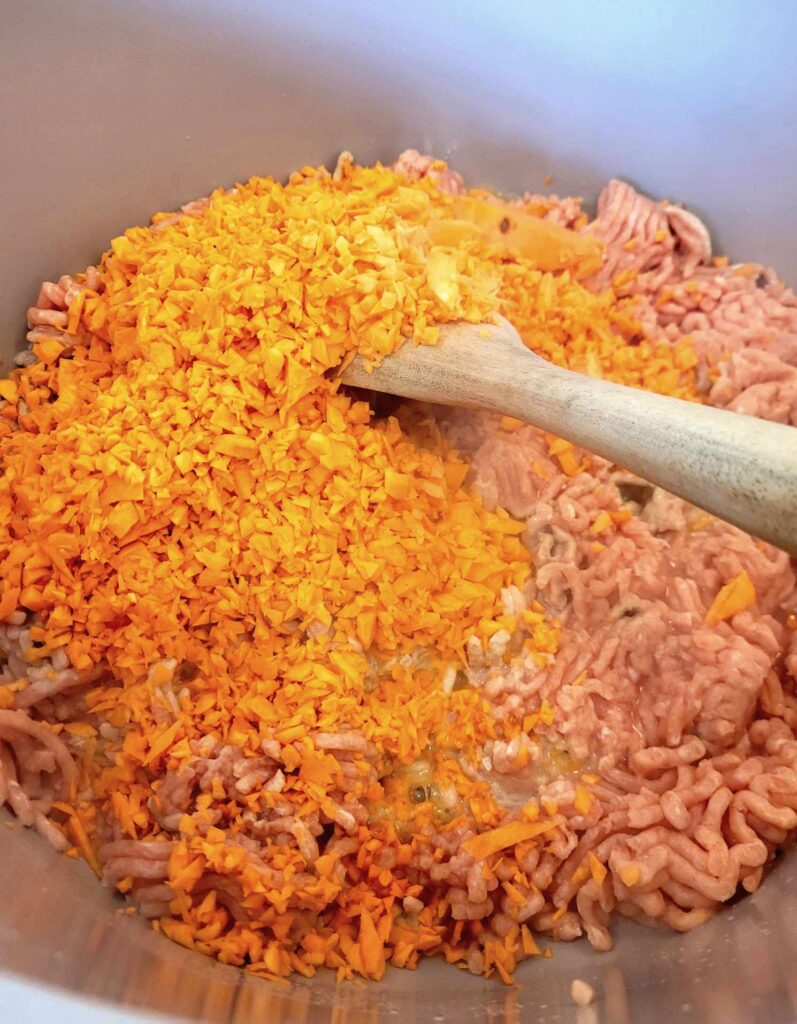 chopped sweet potato and ground chicken cooking in a large skillet making home cooked dog food