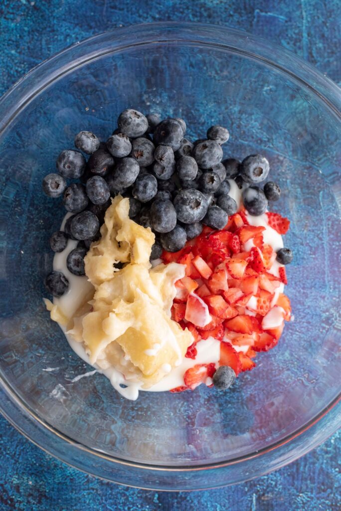 mixing bowl filled with greek yogurt and fresh fruit like blueberries and strawberries for paw print frozen treats
