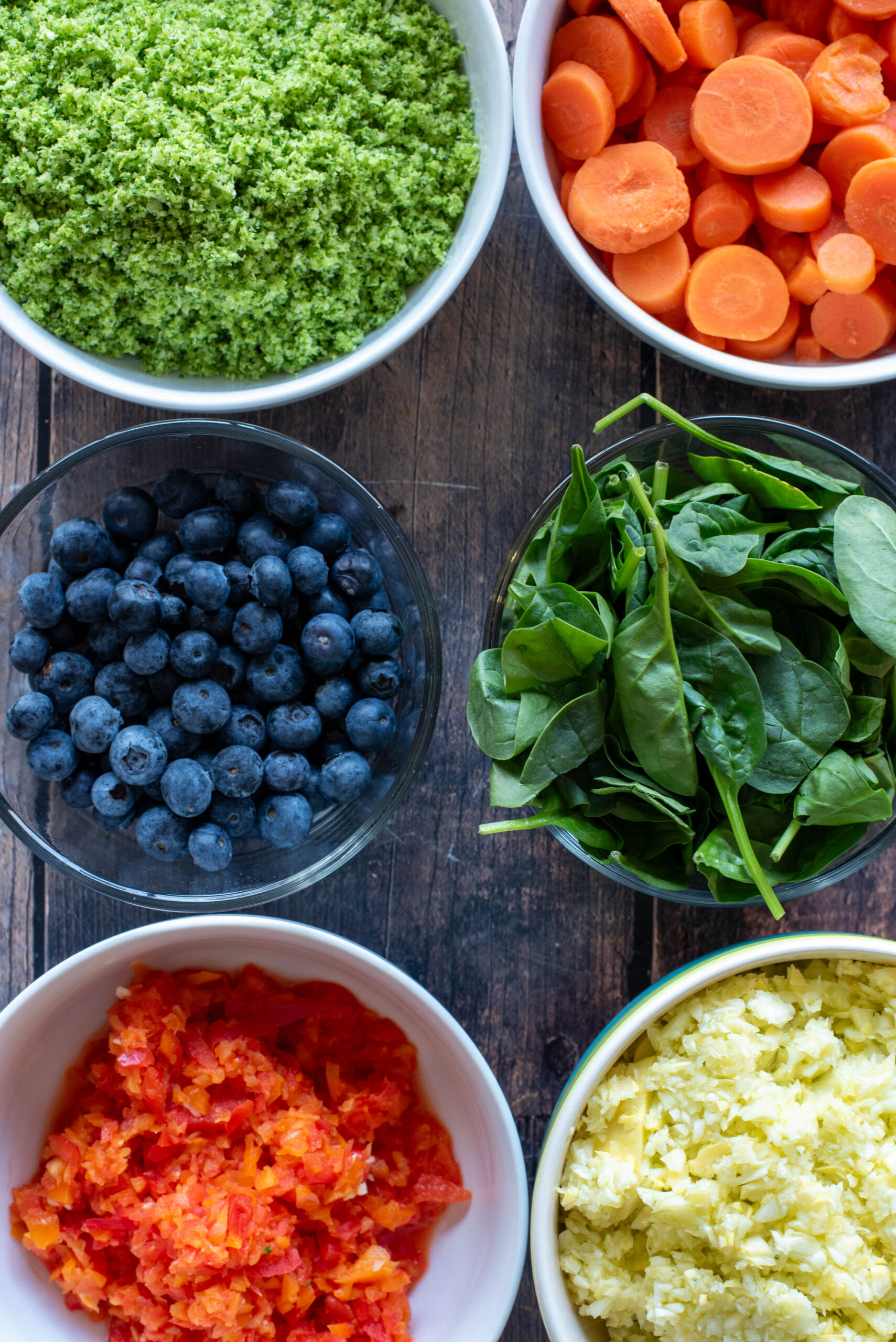 Fresh vegetables and fruit for homemade dog food – carrots, broccoli, spinach, squash, red and orange bell peppers, blueberries arranged on a cutting board."