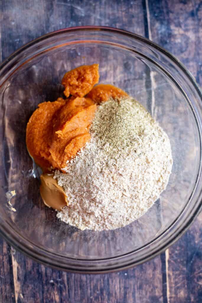 Mixing oat flour, pumpkin puree, peanut butter, and chamomile to form dough for homemade dog calming chews